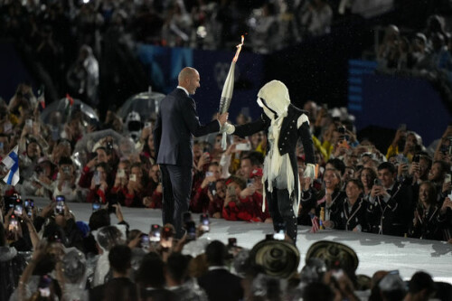 Zinedine Zidane, left, receives the Olympic flame in Paris, France, during the opening ceremony of the 2024 Summer Olympics, Friday, July 26, 2024. (AP Photo/Robert F. Bukaty)